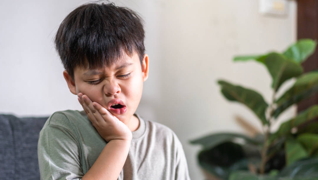 Seorang anak sedang menahan nyeri sakit gigi.