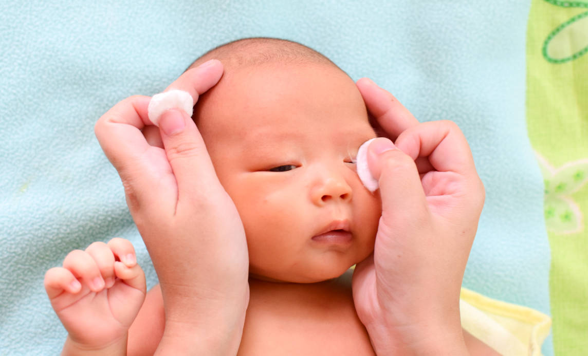 Seorang ibu sedang membersihkan mata bayi dengan kapas